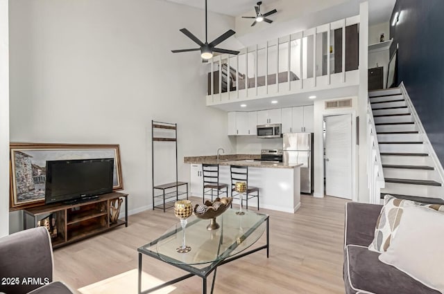 living room with ceiling fan, a towering ceiling, and light wood-type flooring