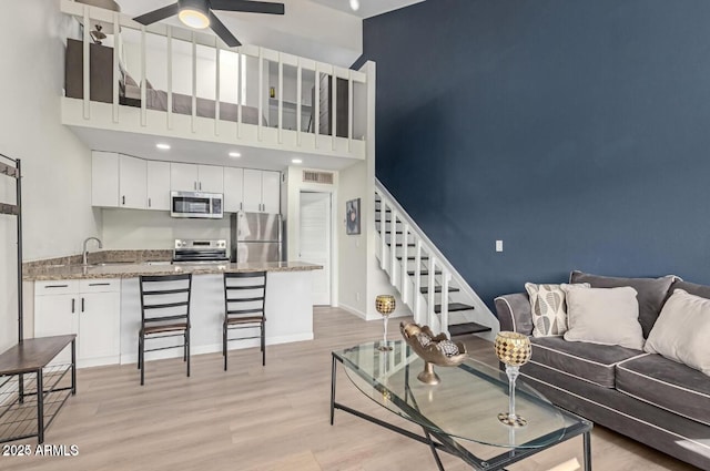 living room with ceiling fan, sink, a high ceiling, and light hardwood / wood-style floors