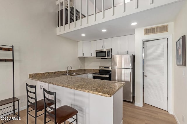 kitchen with kitchen peninsula, sink, stainless steel appliances, and white cabinetry