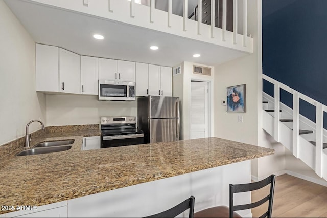 kitchen featuring kitchen peninsula, stainless steel appliances, a kitchen breakfast bar, white cabinets, and sink