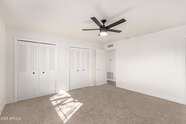 unfurnished bedroom featuring two closets, ceiling fan, and carpet