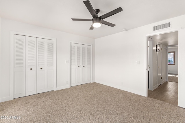 unfurnished bedroom with multiple closets, dark colored carpet, and ceiling fan