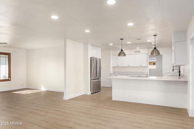 kitchen featuring stainless steel refrigerator, white cabinetry, light hardwood / wood-style floors, and pendant lighting