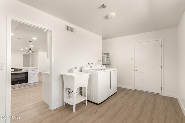 laundry room with water heater, light wood-type flooring, and washer and clothes dryer