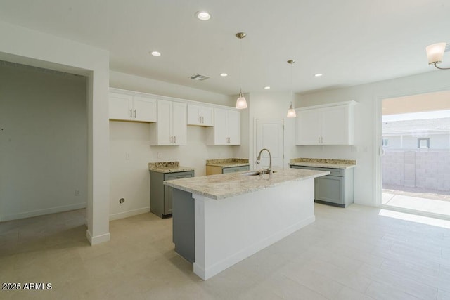 kitchen featuring sink, pendant lighting, white cabinets, and an island with sink