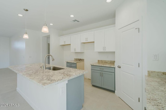 kitchen featuring decorative light fixtures, sink, white cabinets, and an island with sink