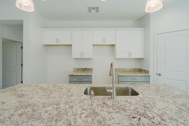 kitchen with white cabinetry, light stone counters, decorative light fixtures, and sink