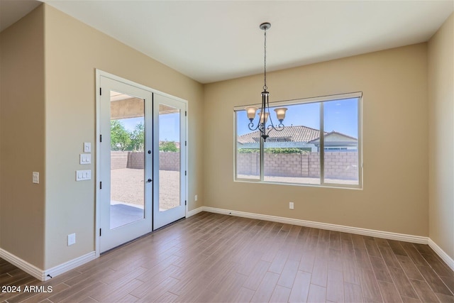 unfurnished dining area featuring a notable chandelier, wood-type flooring, and french doors