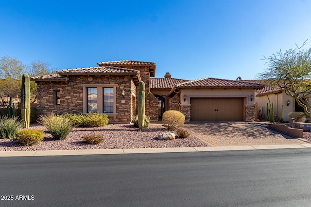 mediterranean / spanish-style home featuring stone siding, a tile roof, an attached garage, decorative driveway, and stucco siding