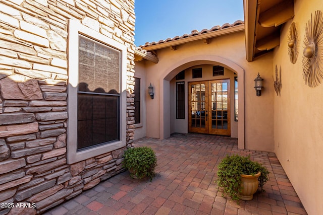 doorway to property featuring french doors, stucco siding, a patio area, stone siding, and a tiled roof