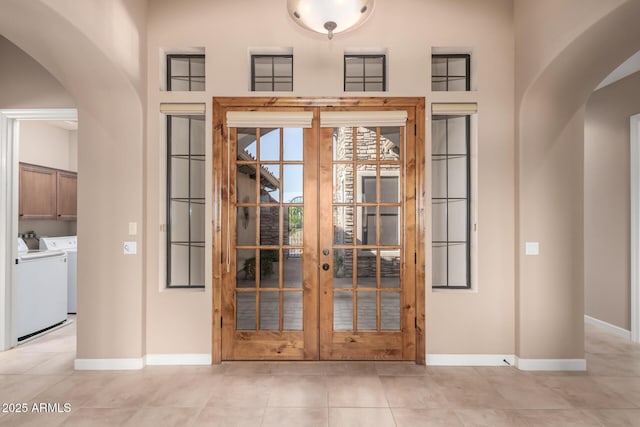 entryway with arched walkways, french doors, washer and clothes dryer, light tile patterned flooring, and baseboards