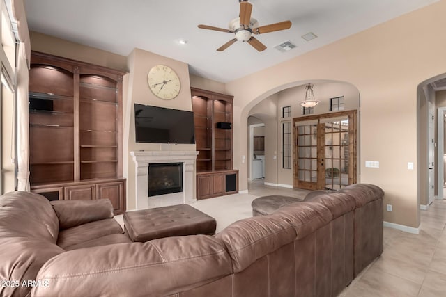 living area with light tile patterned flooring, visible vents, baseboards, a ceiling fan, and a glass covered fireplace