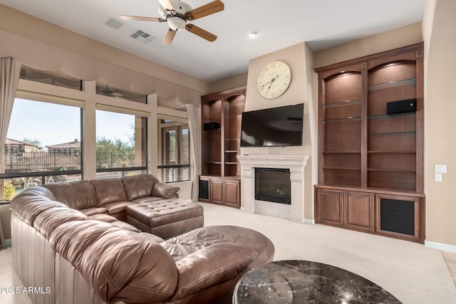 living area featuring light carpet, visible vents, baseboards, a glass covered fireplace, and ceiling fan