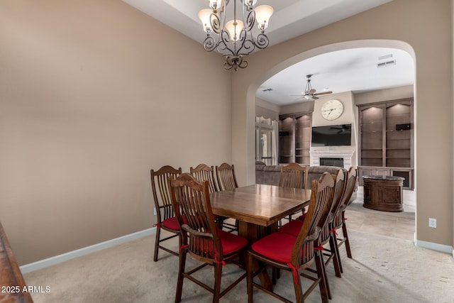 dining room with ceiling fan with notable chandelier, a fireplace, arched walkways, and light colored carpet