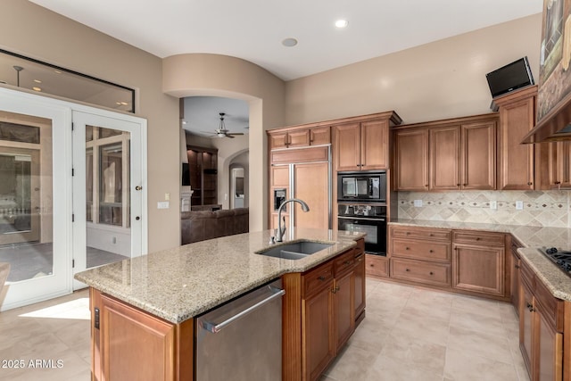 kitchen featuring arched walkways, brown cabinets, backsplash, a sink, and black appliances