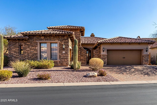 mediterranean / spanish house with decorative driveway, stucco siding, a garage, stone siding, and a tiled roof