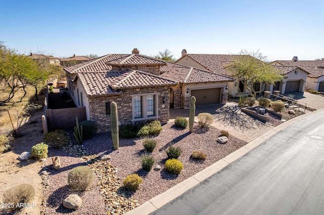 mediterranean / spanish house featuring an attached garage, a tiled roof, stone siding, decorative driveway, and stucco siding