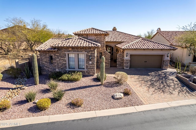 mediterranean / spanish house with a chimney, decorative driveway, a tiled roof, and an attached garage