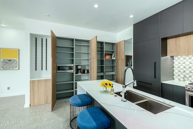 kitchen with stainless steel appliances, light stone countertops, sink, and a breakfast bar area