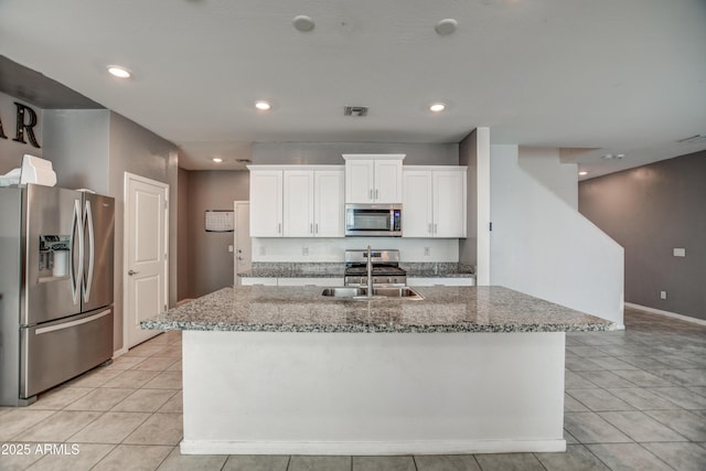 kitchen with white cabinetry, light stone countertops, stainless steel appliances, and an island with sink