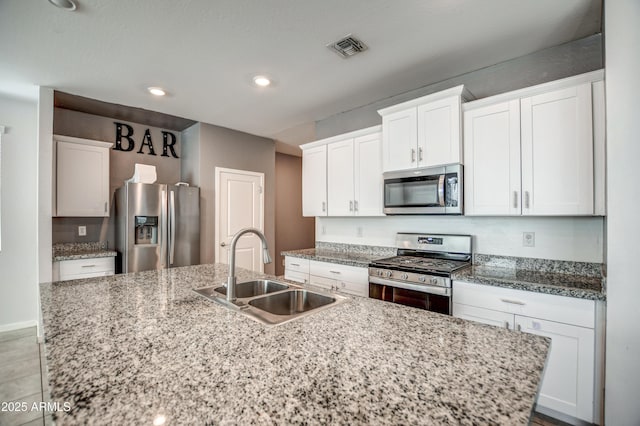 kitchen with sink, stainless steel appliances, light stone countertops, an island with sink, and white cabinets