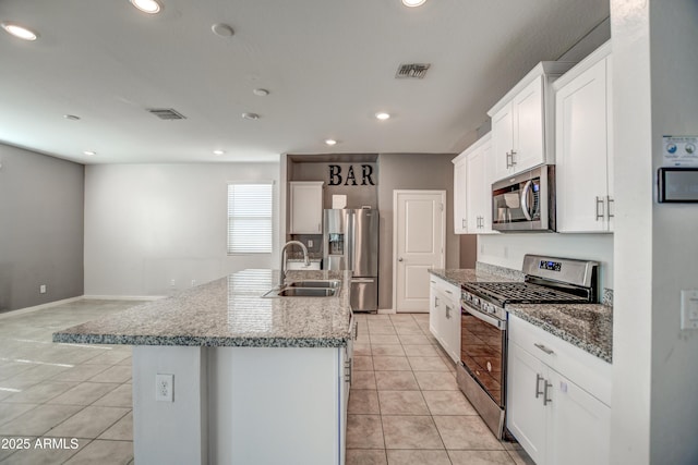 kitchen with stone countertops, white cabinetry, sink, stainless steel appliances, and a center island with sink