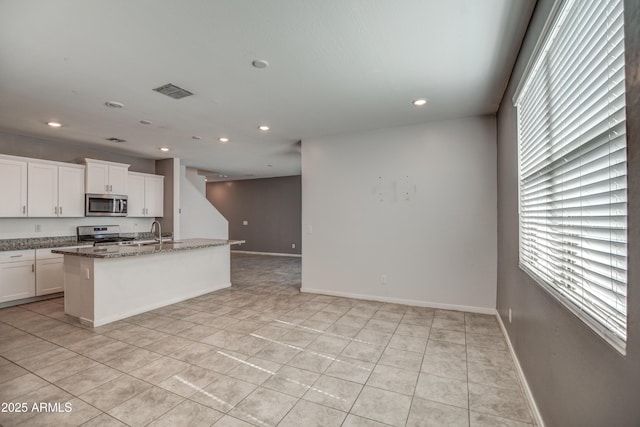 kitchen featuring sink, white cabinetry, dark stone countertops, appliances with stainless steel finishes, and an island with sink