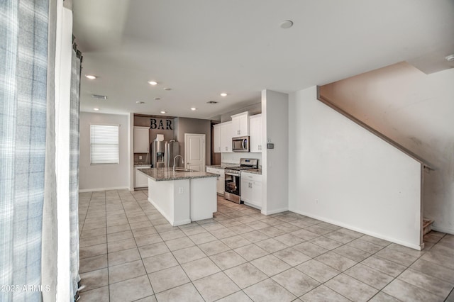 kitchen with sink, a center island with sink, stainless steel appliances, white cabinets, and stone countertops