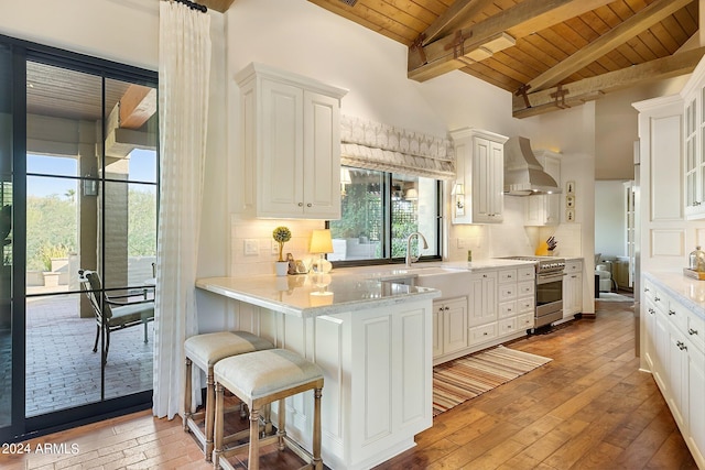 kitchen with wall chimney exhaust hood, stainless steel range, white cabinetry, and wooden ceiling