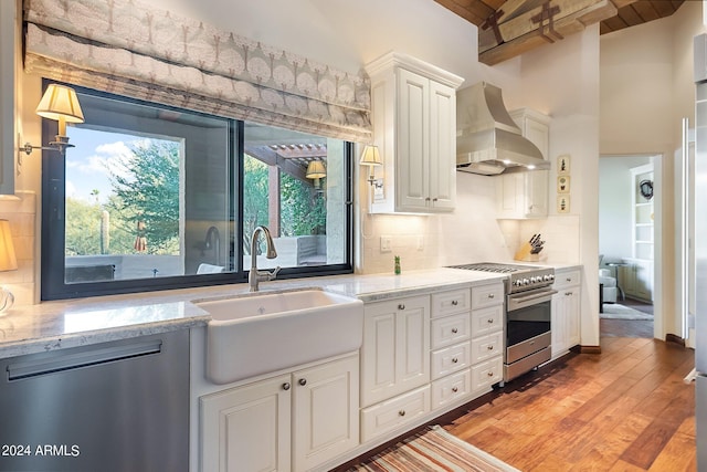 kitchen featuring light wood-type flooring, wall chimney exhaust hood, sink, white cabinetry, and appliances with stainless steel finishes