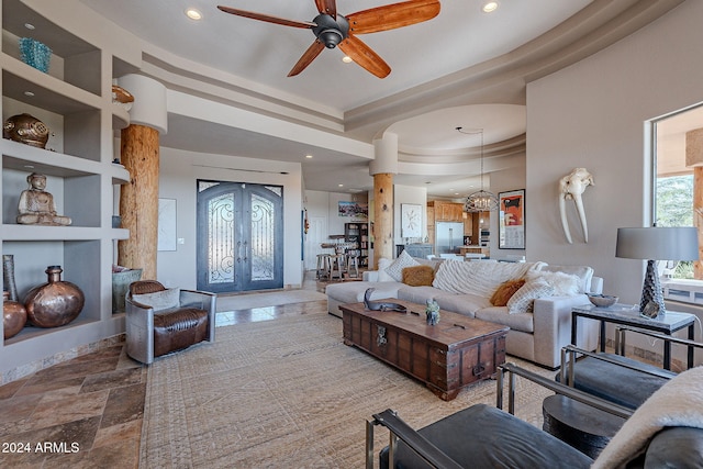 living room featuring french doors, a tray ceiling, ceiling fan with notable chandelier, and built in shelves