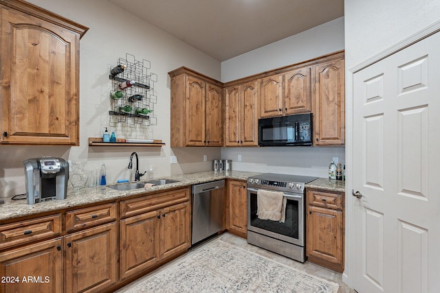 kitchen with appliances with stainless steel finishes, light stone countertops, and sink