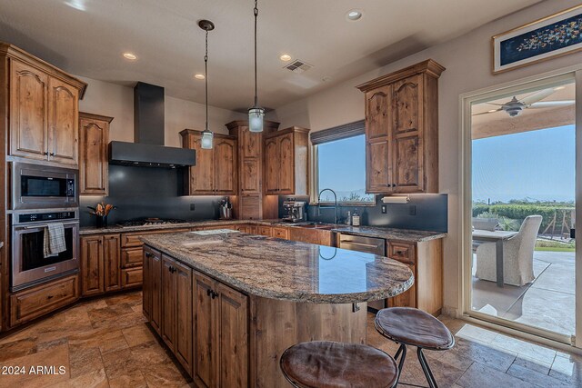 kitchen featuring wall chimney range hood, hanging light fixtures, appliances with stainless steel finishes, sink, and a center island