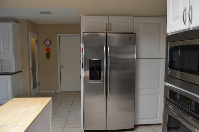 kitchen with appliances with stainless steel finishes, light tile patterned floors, and white cabinetry