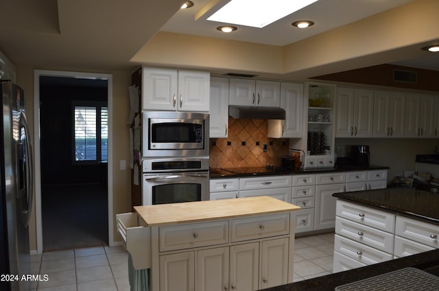 kitchen with a skylight, light tile patterned floors, white cabinets, a kitchen island, and appliances with stainless steel finishes