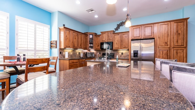 kitchen with stainless steel fridge with ice dispenser, dark stone countertops, decorative light fixtures, and decorative backsplash