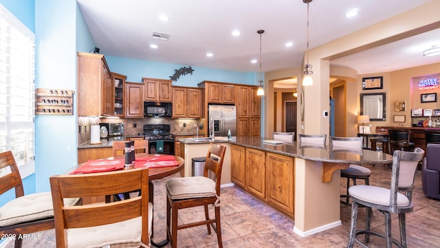 kitchen featuring hanging light fixtures, a kitchen island with sink, black appliances, and dark stone countertops