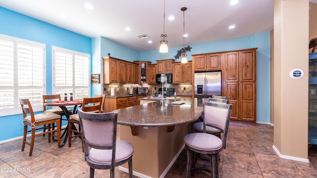 kitchen featuring decorative light fixtures, a kitchen bar, stainless steel refrigerator with ice dispenser, decorative backsplash, and a kitchen island with sink