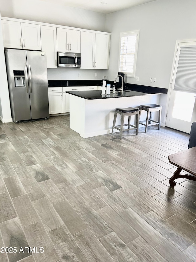 4956 S Leisure Way, Gilbert, AZ 85298 - kitchen featuring appliances with stainless steel finishes, dark countertops, light wood-style flooring, white cabinets, and a peninsula
