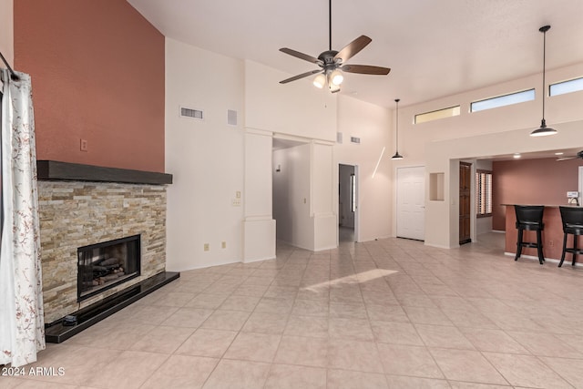 tiled living room with ceiling fan, high vaulted ceiling, and a stone fireplace