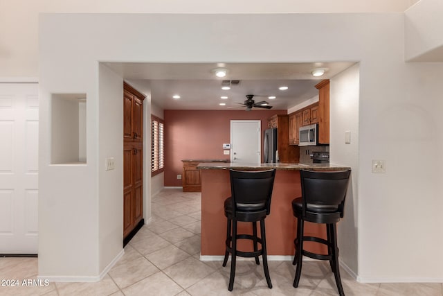 kitchen with a kitchen bar, kitchen peninsula, ceiling fan, stainless steel appliances, and light tile patterned floors