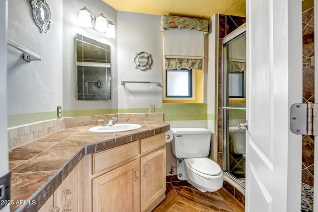 bathroom featuring toilet, a stall shower, vanity, and a textured wall