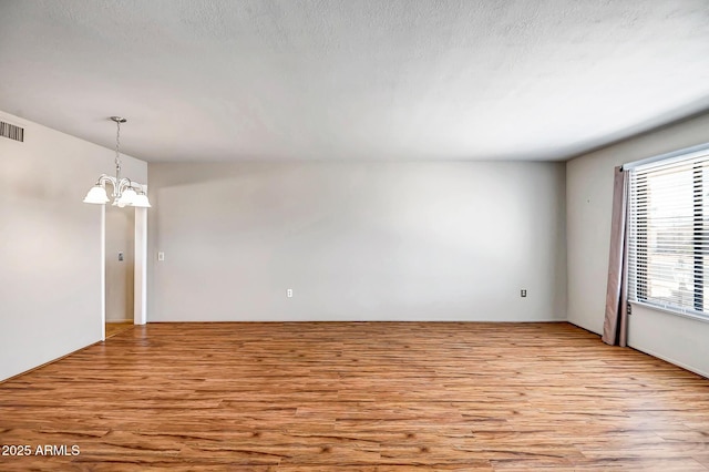 empty room with a textured ceiling, visible vents, light wood finished floors, and a chandelier