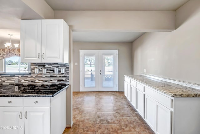 kitchen with a notable chandelier, dark stone countertops, tasteful backsplash, white cabinetry, and french doors