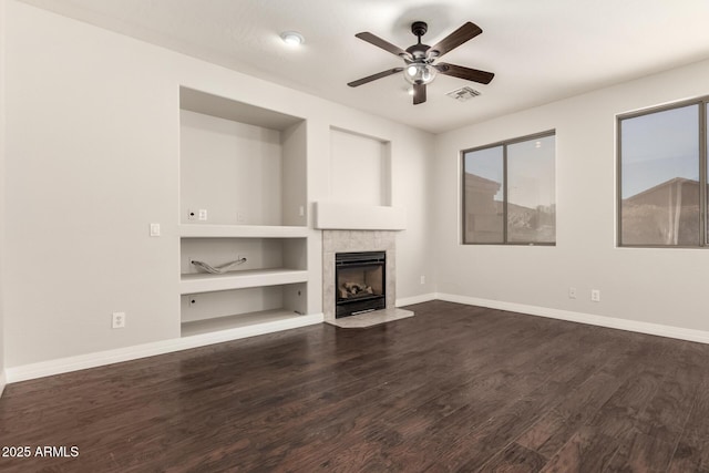 unfurnished living room with built in shelves, a tile fireplace, dark hardwood / wood-style floors, and ceiling fan