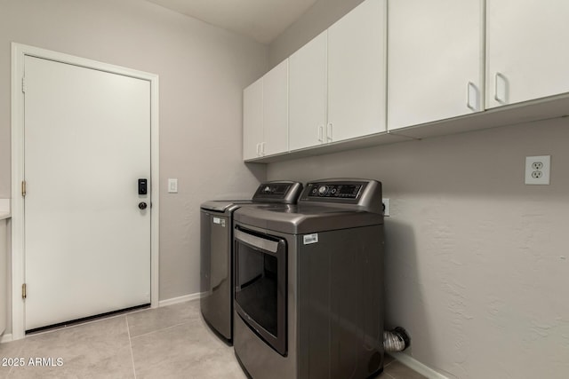 clothes washing area with cabinets, light tile patterned floors, and washing machine and clothes dryer