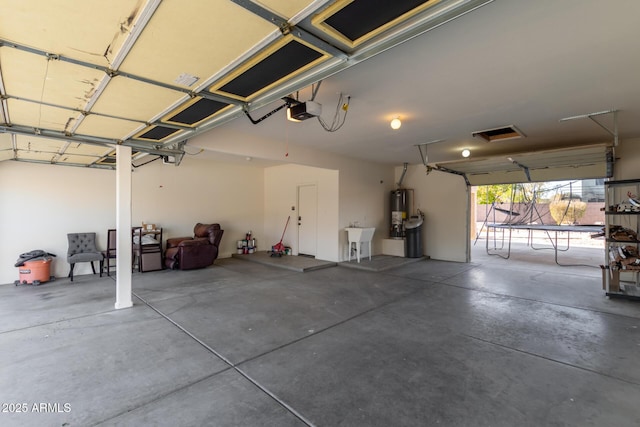 garage with a garage door opener, gas water heater, sink, and a trampoline