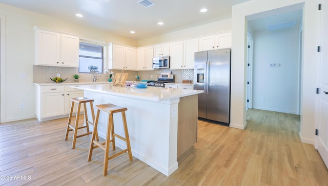 kitchen featuring a kitchen island, a kitchen breakfast bar, light countertops, light wood finished floors, and appliances with stainless steel finishes