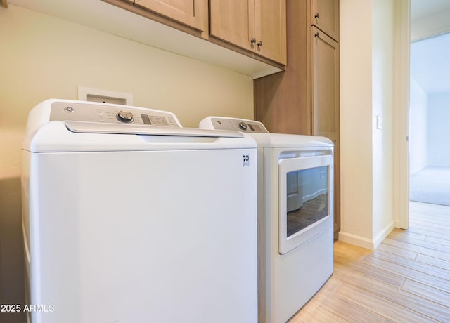 washroom featuring baseboards, cabinet space, light wood-style flooring, and independent washer and dryer