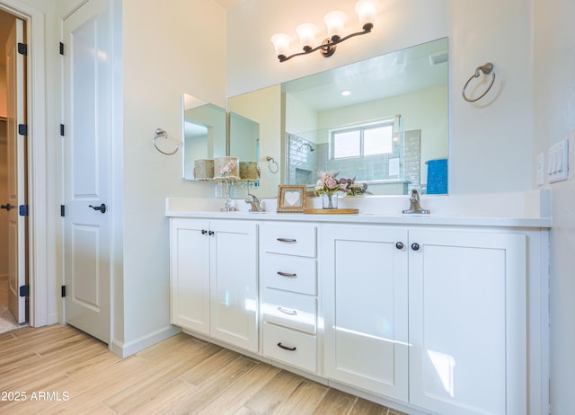 bathroom with double vanity, walk in shower, a sink, and wood finished floors